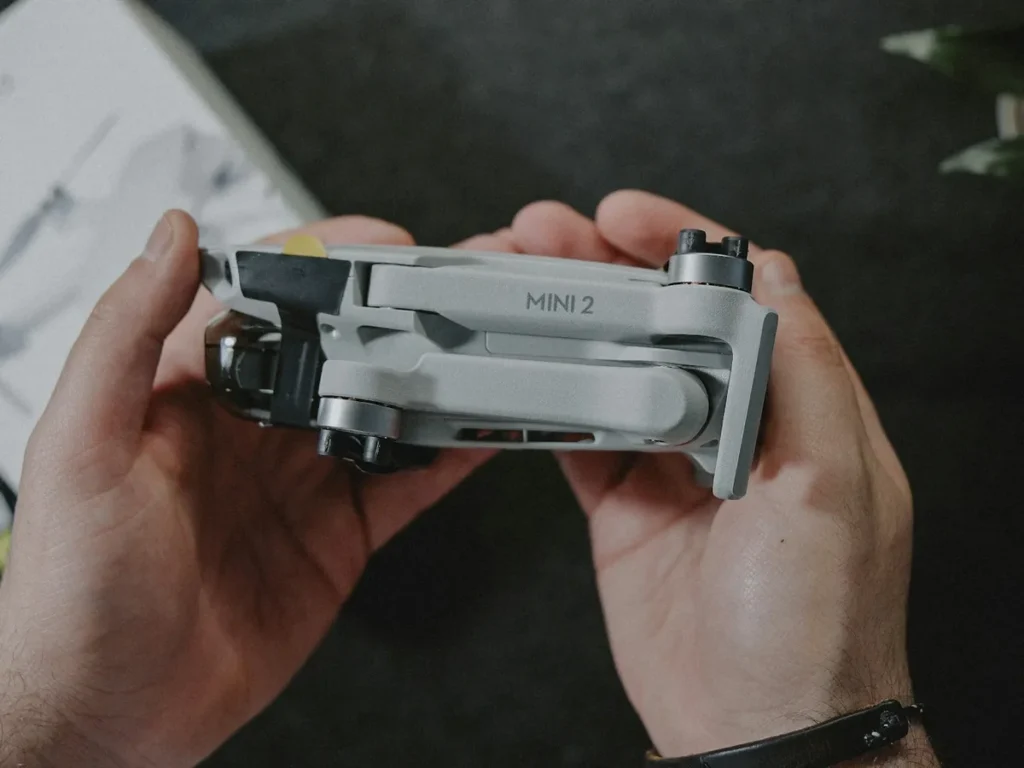 Mão segurando um drone DJI dobrado ao lado da caixa e do manual
