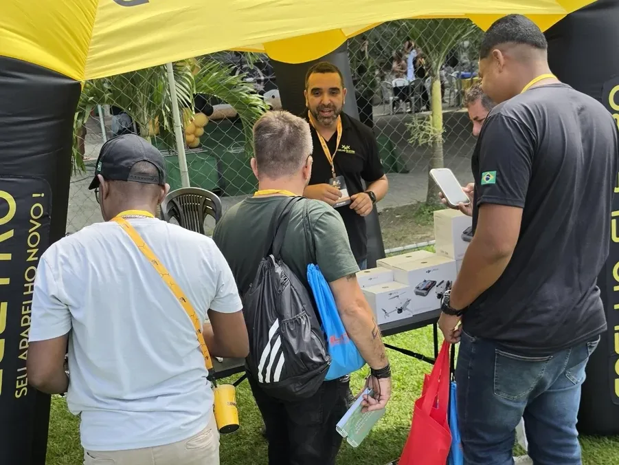 Equipe da Coelho Eletro atendendo visitantes na mesa de drones DJI sob a tenda amarela