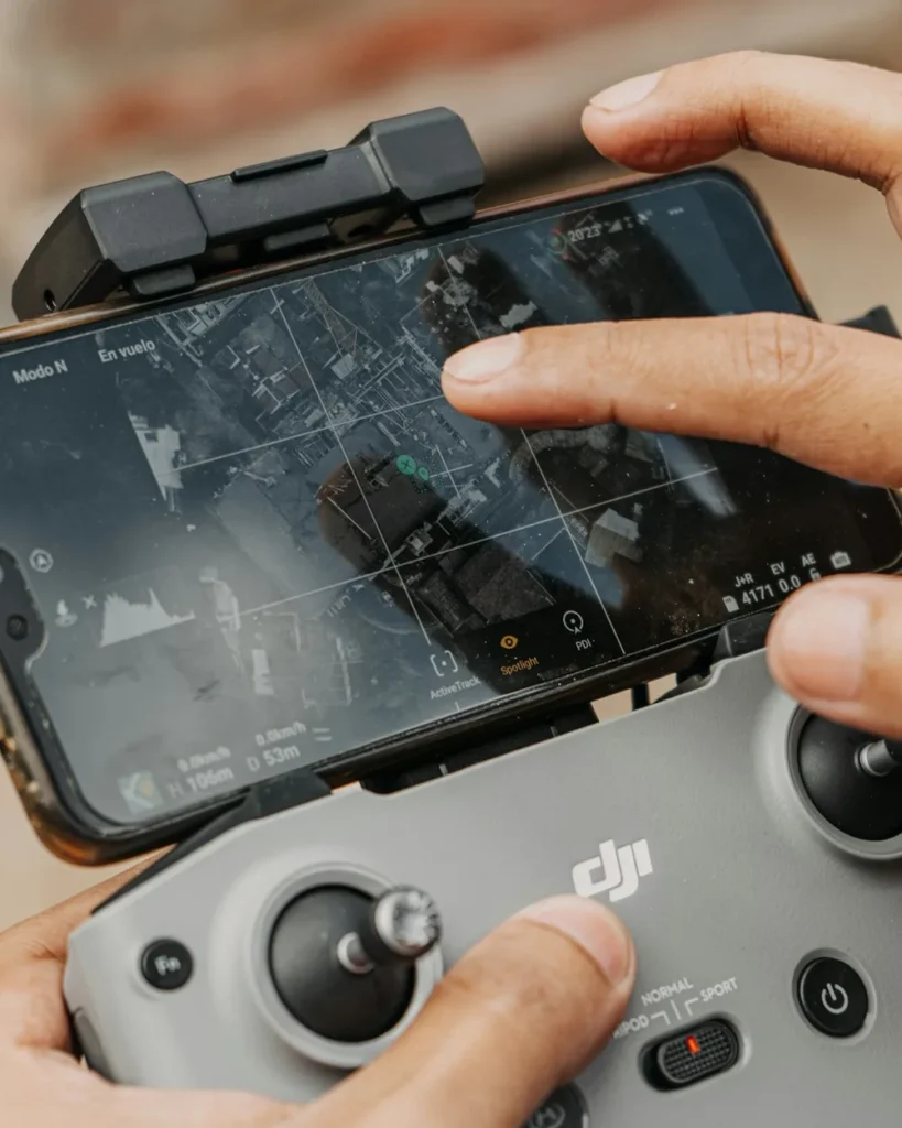 Mãos de um piloto usando o controle DJI com o celular mostrando o mapa de voo