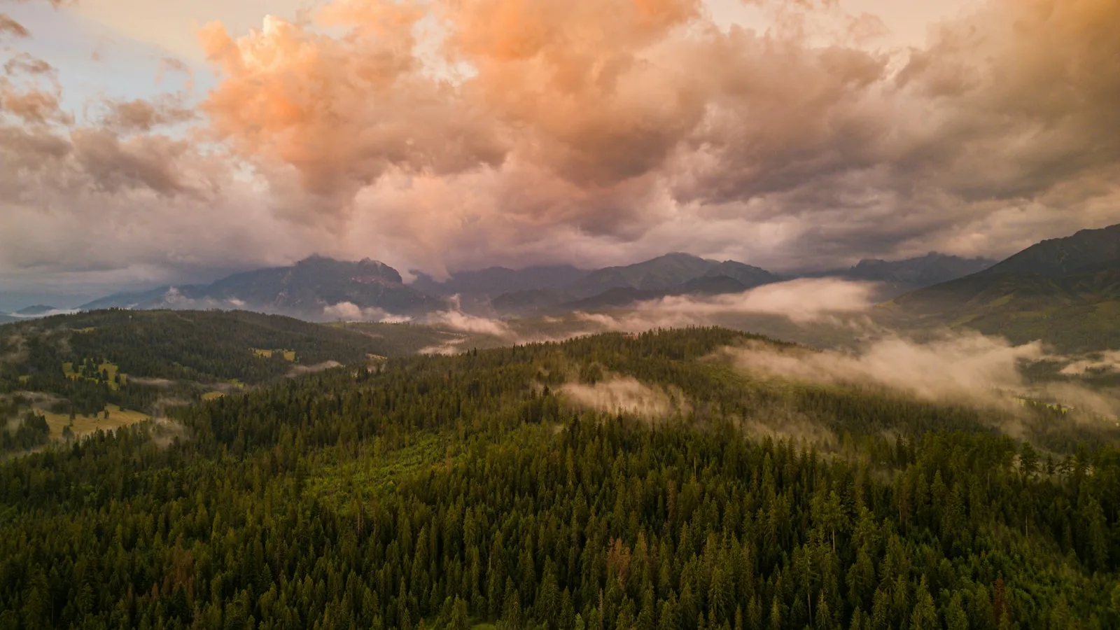 Fotografia aérea de montanhas cobertas de floresta com nuvens alaranjadas ao pôr do sol