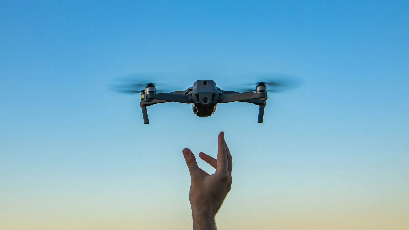 Drone pairando logo acima da mão do piloto com céu ao entardecer