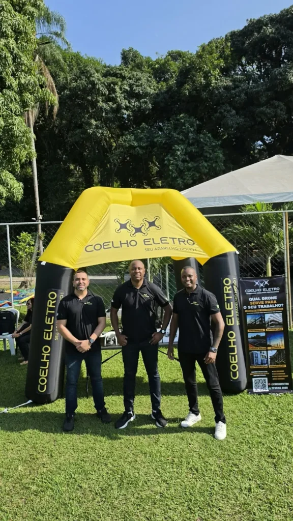 Equipe da Coelho Eletro posando em frente à tenda amarela da loja em um evento ao ar livre